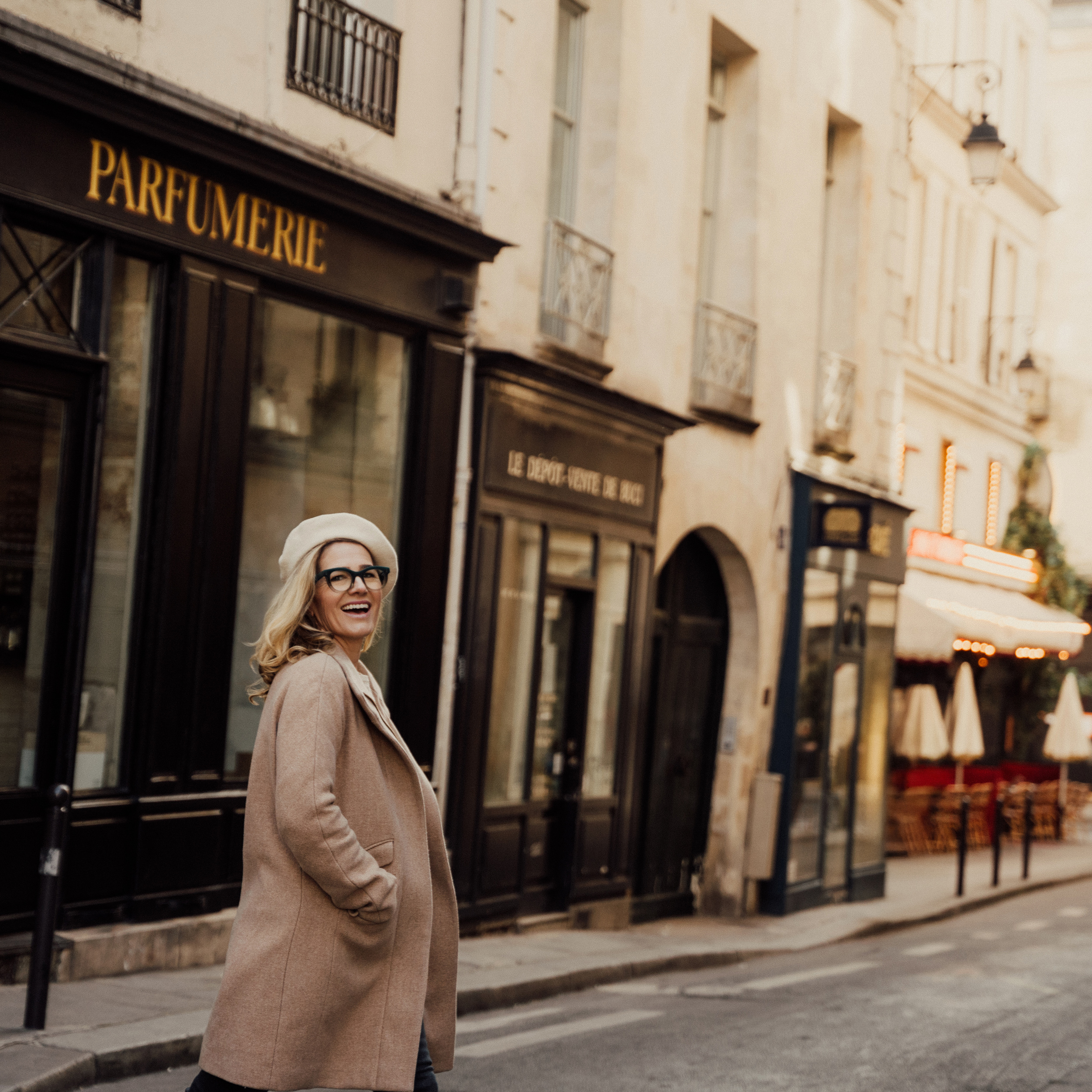 young woman in a long coat and beret crosses a Parisian street